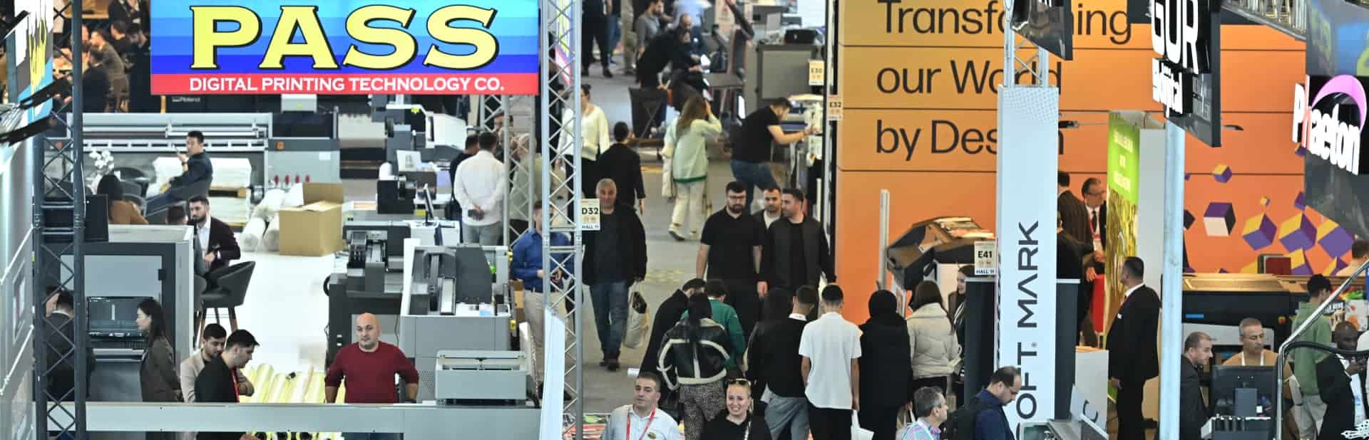 Exhibition floor with people walking and exploring various digital printing stands including PASS and HP