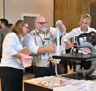  Exhibitors demonstrating textile printing techniques using a heat press machine at SIGN İstanbul