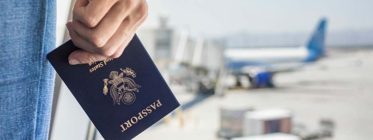 Havalimanında, arka planda uçak ve bagajlarla birlikte bir pasaportu tutan elin yakın çekimi.